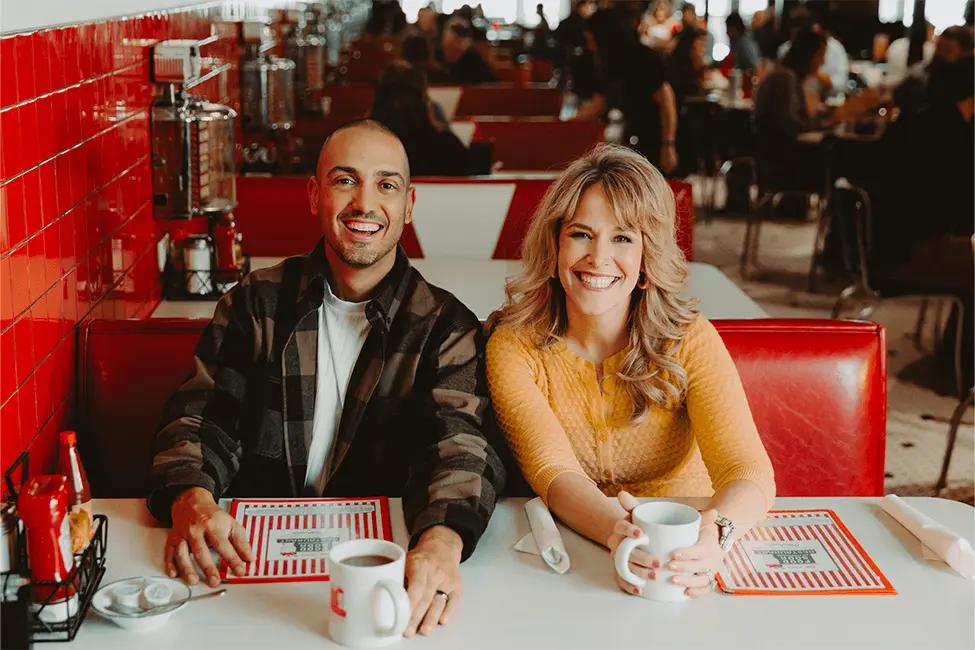 DJs Carlos and Amy sitting at a diner table