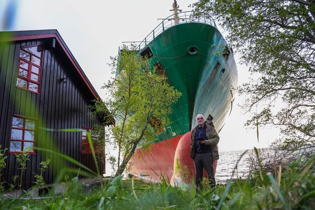 Johan Helberg stands next to his house, with the container ship NCL Salten in the background