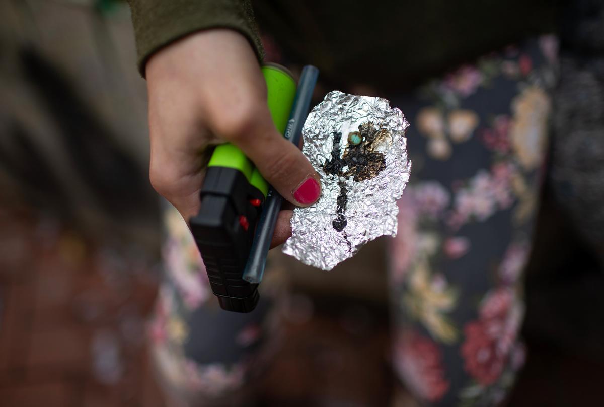 A woman holds drug paraphernalia, including a vape pen and black tar heroin in a piece of tinfoil