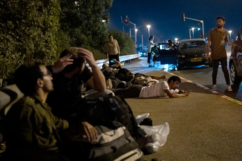 Israelis take cover as projectiles launched from Iran are being intercepted in the skies over in Rosh HaAyin, Israel, Tuesday, Oct. 1, 2024. 