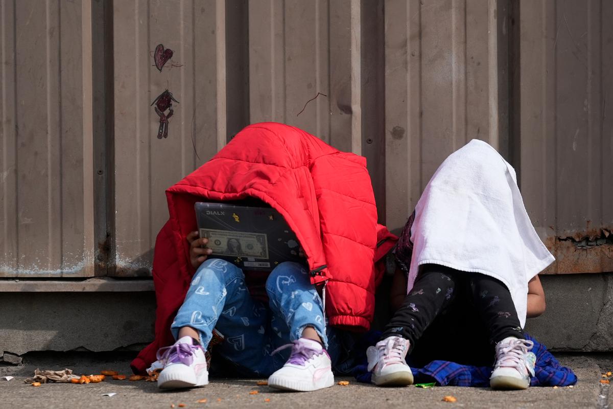 Two small children sitting with coats over their heads.