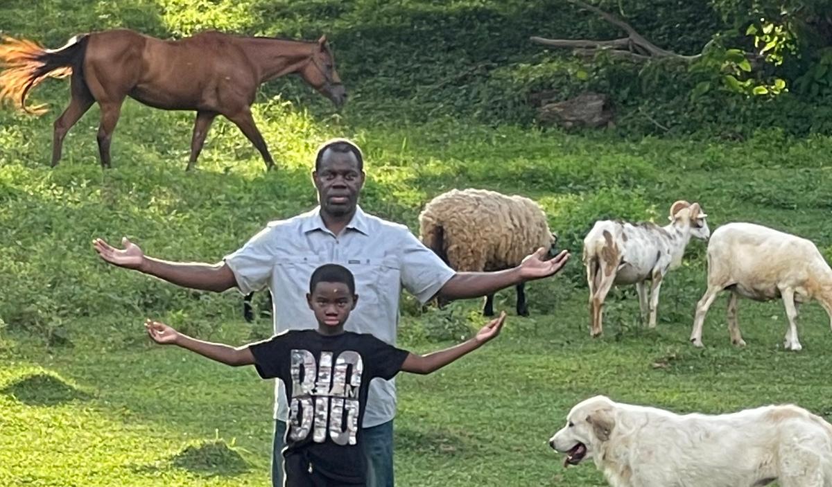 Father and son with arms out and animals in the background